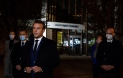 French President Emmanuel Macron, flanked by offcials, speaks to the press following a stabbing attack at a school in the Conflans-Sainte-Honorine suburb of Paris, France, Oct. 16, 2020.