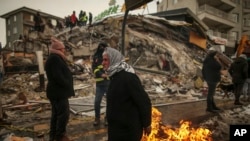 ARCHIVO - La gente se calienta junto a un edificio derrumbado en Malatya, Turquía, en febrero de 2023.