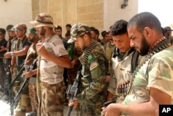 FILE - Newly arrived Iraqi Shi'ite militiamen check their weapons in the predominately Sunni city of Nukhayb, in southwest Iraq, May 21, 2015. Analysts fear deep sectarian divisions will cripple the fight against the Islamic State group.