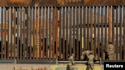 Los soldados estadounidenses caminan junto a la cerca fronteriza entre México y Estados Unidos, mientras se observa a los migrantes caminando detrás de la cerca, luego de cruzar ilegalmente a EE.UU. para entregarse en El Paso, Texas.