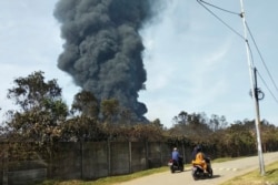 Pengendara motor melewati kepulan asap pekat akibat kebakaran kilang Balongan milik PT Pertamina, Indramayu,Jawa Barat, 29 Maret 2021. Ratusan orang dievakuasi dari desa terdekat setelah kebakaran besar terjadi di kilang tersebut. (Foto AP)