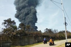 Pengendara motor melewati kepulan asap pekat akibat kebakaran kilang Balongan milik PT Pertamina, Indramayu,Jawa Barat, 29 Maret 2021. Ratusan orang dievakuasi dari desa terdekat setelah kebakaran besar terjadi di kilang tersebut. (Foto AP)