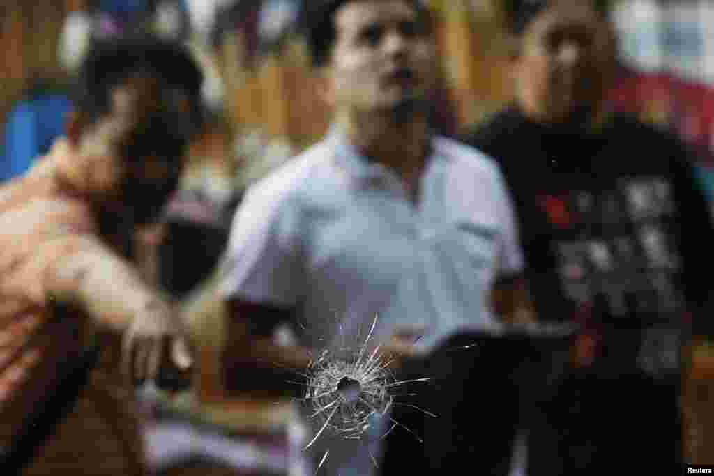 An investigator points at a bullet hole in the window of a cafe after a shooting incident near the Khao San Road tourist area. Seven people were wounded, one seriously, after gunmen opened fire on anti-government protesters, Bangkok, Thailand, Jan. 11, 2014.