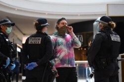 FILE - Victoria Police officers speak with a masked member of the public in a shopping center following an anti-lockdown protest in response to the city's COVID-19 restrictions in Melbourne, Australia, Sept. 20, 2020.