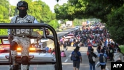 A member of the National Guard escorts migrants walking on an US-bound caravan on the outskirts of Tapachula, State of Chiapas, Mexico on July 23, 2024.