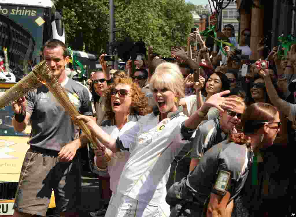 In this photo provided by LOCOG, British actresses Joanna Lumley, center right, and Jennifer Saunders, center left, carry the Olympic Flame between Lambeth and Kensington and Chelsea, in London, July 26, 2012. 
