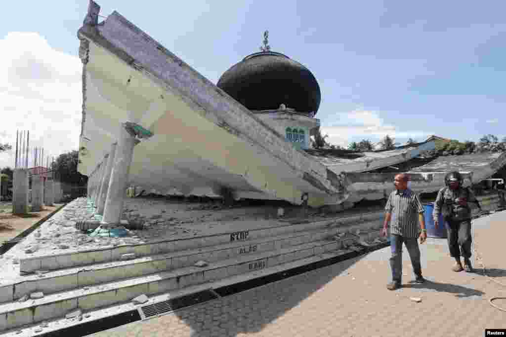 Dua pria berjalan di dekat sebuah masjid yang ambruk akibat gempa bumi di kota Meuredu, Pidie Jaya, Aceh, (Foto: Antara).