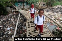 Students cross a bamboo bridge, above a garbage-filled stream branching off the Ciliwung River, in Bogor, Indonesia, September 25, 2018.