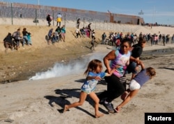 Maria Lila Meza Castro (C), a 39-year-old migrant woman from Honduras, runs away from tear gas with her five-year-old twin daughters Saira Nalleli Mejia Meza (L) and Cheili Nalleli Mejia Meza (R) in front of the border wall between the U.S and Mexico, in Tijuana, Nov. 25, 2018.