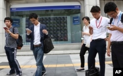 People look at their smartphones in front of an electronic stock board of a securities firm in Tokyo, Aug. 28, 2017.