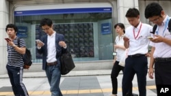 People look at their smartphones in front of an electronic stock board of a securities firm in Tokyo, Monday, Aug. 28, 2017. (AP Photo/Koji Sasahara)