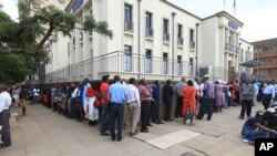 In this photo taken on Tuesday, May, 3, 2016, Zimbabweans wait in a long line to withdraw cash in Harare. Severe shortages of U.S dollars that are used as local currency have forced many residents into cash hunter-gatherers.