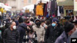 Para pejalan kaki, beberapa mengenakan masker bedah, yang lain masker FFP2, berjalan melewati kios-kios di pasar terbuka Porta Portese, Roma, 9 Januari 2022. (AP/Gregorio Borgia)