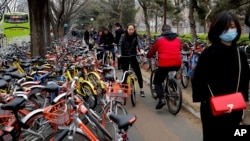 Residents ride bicycles from bike-sharing company Ofo try to pedal through a sidewalk crowded with bicycles from the bike-sharing companies Ofo, Mobike and Bluegogo, near a bus stand in Beijing, China, March 23, 2017. As many as 2.2 million of these two-w