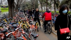 Residents ride bicycles from bike-sharing company Ofo try to pedal through a sidewalk crowded with bicycles from the bike-sharing companies Ofo, Mobike and Bluegogo, near a bus stand in Beijing, China, March 23, 2017.