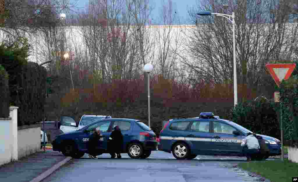 French security officers take cover behind vehicles as they surround a building in Dammartin-en-Goele, northeast of Paris, where the two brothers suspected in a deadly terror attack were cornered, Jan. 9, 2015.