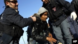 A man (c) who fled the unrest in Tunisia is helped by the Italian police after arriving at the southern Italian island of Lampedusa March 24, 2011