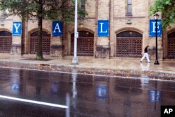 FILE - A woman walks by a Yale sign reflected in the rainwater on the Yale University campus in New Haven, Connecticut, Aug. 22, 2021.