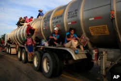 A woman holding her baby hitches a ride on the fender of a tanker in Niltepec, Mexico, Oct. 30, 2018.