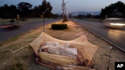 FILE - Vehicles move past Pakistani day laborers sleeping under a mosquito net in the middle of a road in Islamabad, Pakistan.