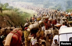 FILE - Rwandese refugees cross Rusumo border to Tanzania from Rwanda carrying their belongings even goats, mattresses and cows, May 30, 1994.