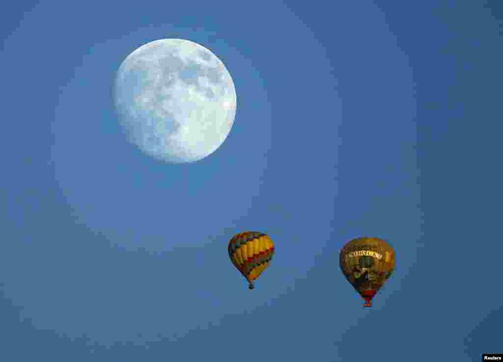 Hot air balloons makes their way past the rising moon as the sun sets near Encinitas, California, USA, Sept. 6, 2014.