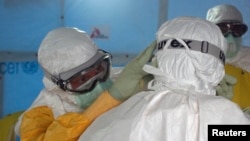 Một bác sĩ Mỹ trong trang phục bảo hộ PPE giúp một đồng nghiệp điều chỉnh lại bộ bảo hộ trước khi đi vào một đơn vị điều trị Ebola ở Monrovia, Liberia.