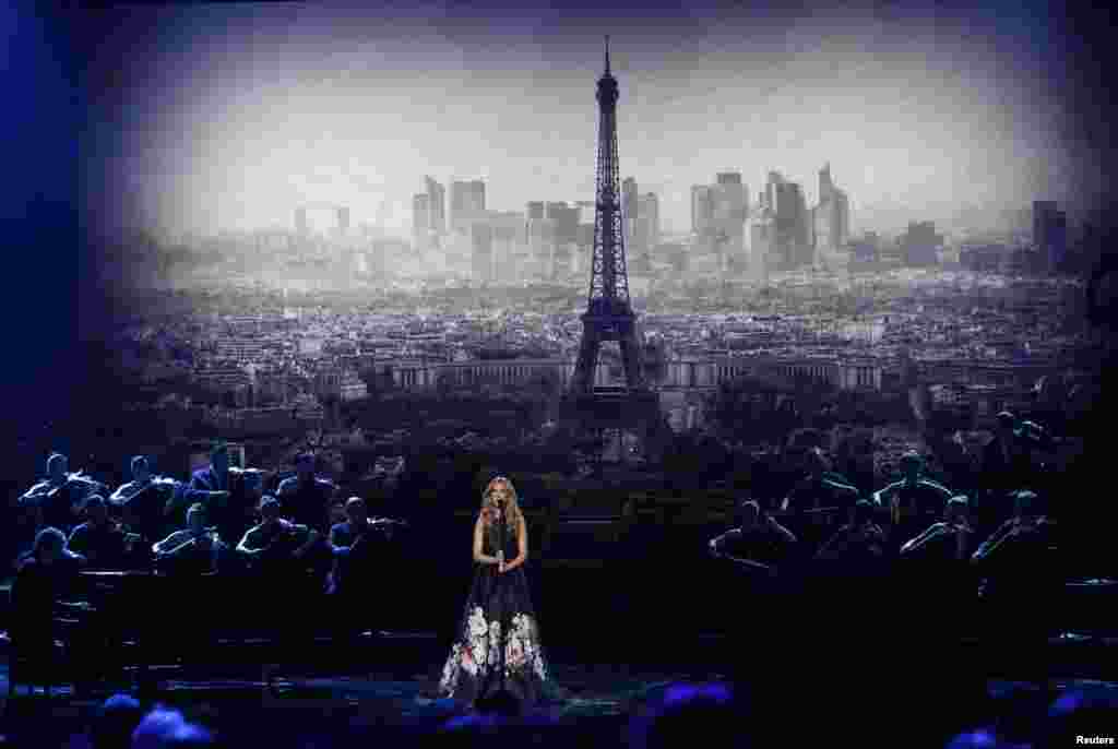 Celine Dion oo qaadeysa heesta &quot;Hymne a l&#39;amour&quot;, ayada oo ku xuseysa dhibanayaasha weeraradii Paris, xilli sawirka taallada Paris uu gadaasheeda ka muuqdo.