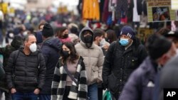 People, some wearing surgical masks, others FFP2 masks, to cope with the surge of COVID-19 cases stroll past stalls at the Porta Portese open air market, in Rome, Jan. 9, 2022. 