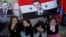 Syrian women sit under a flag with a portrait of President Bashar Assad during constitutional referendum, Damascus, Feb. 26, 2012 (file photo).