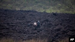 Men chat amid a band of harden lava that flowed from the Pacaya Volcano, near El Patrocinio village in San Vicente Pacaya, Guatemala, April 21, 2021.