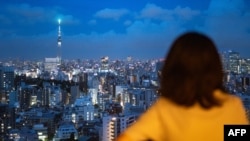 FILE - A woman looks at the city skyline with clouds in the distance at dusk from the Bunkyo Civic Center Observation Deck in Tokyo on August 28, 2024.