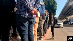People seeking asylum in the United States wait at the border crossing in Tijuana, Mexico, Jan. 8, 2020, just across the border from San Diego. The number of people arrested or stopped entering the U.S. along the Mexico border fell for a seventh month.