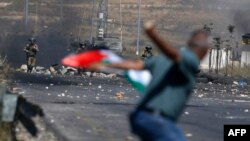 Un manifestant palestinien lance une pierre en direction des forces israéliennes lors d'affrontements près de la colonie juive de Beit El, près de Ramallah, en Cisjordanie occupée, le 14 mai 2021.