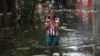 Seorang wanita ketika mengarungi air banjir di Jakarta, Indonesia, Sabtu, 4 Januari 2020. Hujan dan naiknya sungai merendam sebagian wilayah Jakarta dan menyebabkan tanah longsor di kabupaten Bogor dan Depok di pinggiran kota. (Foto: AP)
