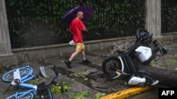 Un hombre pasa junto a un árbol caído y vehículos en medio de fuertes vientos y lluvia por el paso del tifón Bebinca en Shanghai el 16 de septiembre de 2024. AFP