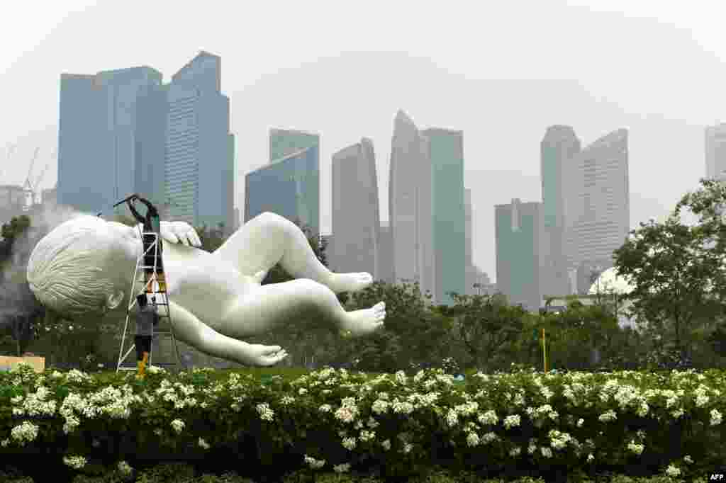 Buildings in the financial district are seen through a blanket of haze from the Garden by the Bay in Singapore, as a worker (L) washes a sculpture by renowned sculptor Marc Quinn of a sleeping boy depicting his infant son, Lucas.