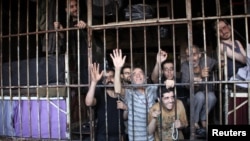 FILE - Inmates gesture from behind bars in Aleppo's main prison May 22, 2014. A recent coalition airstrike on an IS-run prison in the eastern Syrian town of al-Mayadeen reportedly killed 57 people.