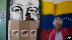 Un hombre emite su voto frente a un mural del fallecido presidente Hugo Chávez como parte de un ensayo para las elecciones presidenciales del 28 de julio en un centro de votación en Caracas, Venezuela, el domingo 30 de junio de 2024. (Foto AP/Cristian Hernandez Fortune)