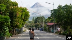 Seorang perempuan yang menggendong anaknya tampak mengamati gunung berapi Mayon di Legazpi, provinsi Albay, Filipina, pada 13 Juni 2023. (Foto: AP/Aaron Favila)