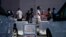 FILE - A sign indicates where mail ballots may dropped off as people wait in line at one of the few in-person voting places during a nearly all-mail primary election in Las Vegas, June 9, 2020.