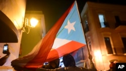 Protesters hold a Puerto Rican flag in San Juan, Puerto Rico, Jan. 23, 2020. Hundreds of people joined a demonstration reminiscent of those that ousted the island's governor last year. Anger is growing over emergency aid that had sat unused.