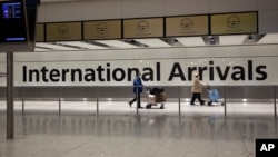 FILE - In this Jan. 26, 2021 file photo, arriving passengers walk past a sign in the arrivals area at Heathrow Airport in London, during England's third national lockdown since the coronavirus outbreak began. 