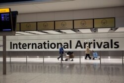 FILE - In this Jan. 26, 2021 file photo, arriving passengers walk past a sign in the arrivals area at Heathrow Airport in London, during England's third national lockdown since the coronavirus outbreak began.