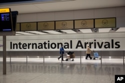 FILE - In this Jan. 26, 2021 file photo, arriving passengers walk past a sign in the arrivals area at Heathrow Airport in London, during England's third national lockdown since the coronavirus outbreak began.