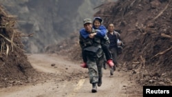 2013年4月22日，在宝兴县灵官镇外的一条刚刚被清理出来的道路上，一名解放军战士背着一位60岁的老大娘脱离险区。