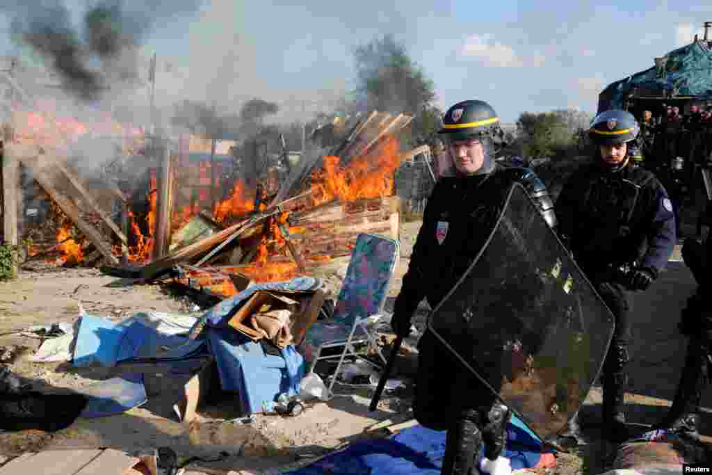 French riot police officer secures the area near a burning makeshift shelter set ablaze in protest against the dismantlement of the camp for migrants called the &quot;Jungle&quot; in Calais on the second day of their evacuation and transfer to reception centers, France.
