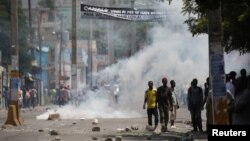 Protesters stand next to tear gas rising up during clashes at a demonstration against the government in Port-au-Prince, Haiti, Sept. 12, 2017.