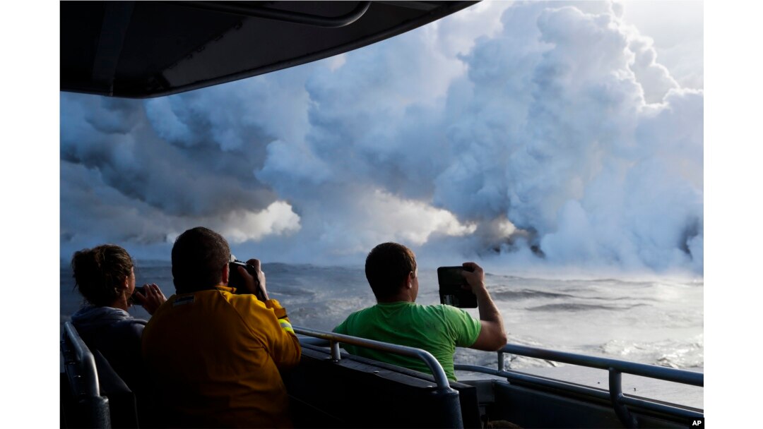 Para wisatawan di kapal mengambil gambar lahar mengalir ke pantai hingga menghasilkan kepulan asap dekat Pahoa, Hawaii, 20 Mei 2018.