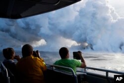 Para wisatawan di kapal mengambil gambar lahar mengalir ke pantai hingga menghasilkan kepulan asap dekat Pahoa, Hawaii, 20 Mei 2018.